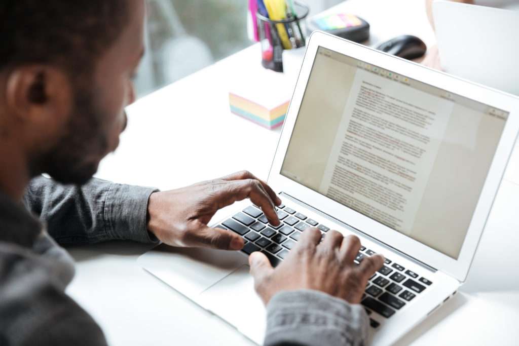 Homem negro sentado em frente ao seu computador enquanto digita um conteúdo elaborado a partir de um briefing 