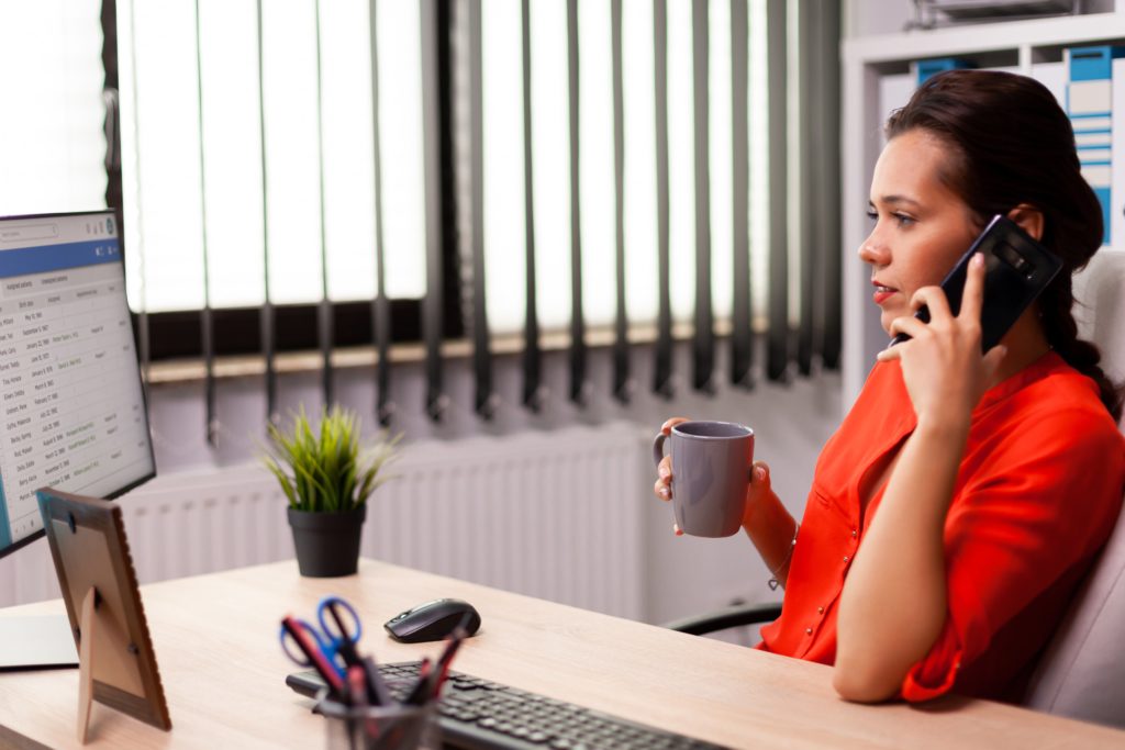 Imagem de uma atendente mulher com um telefone no ouvido enquanto acompanha a tela de um computador de mesa e definindo Estratégias de vendas para varejo