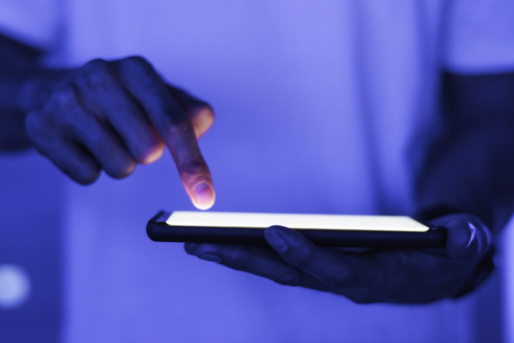 Imagem de alguém segurando um smartphone com um fundo levemente azul 