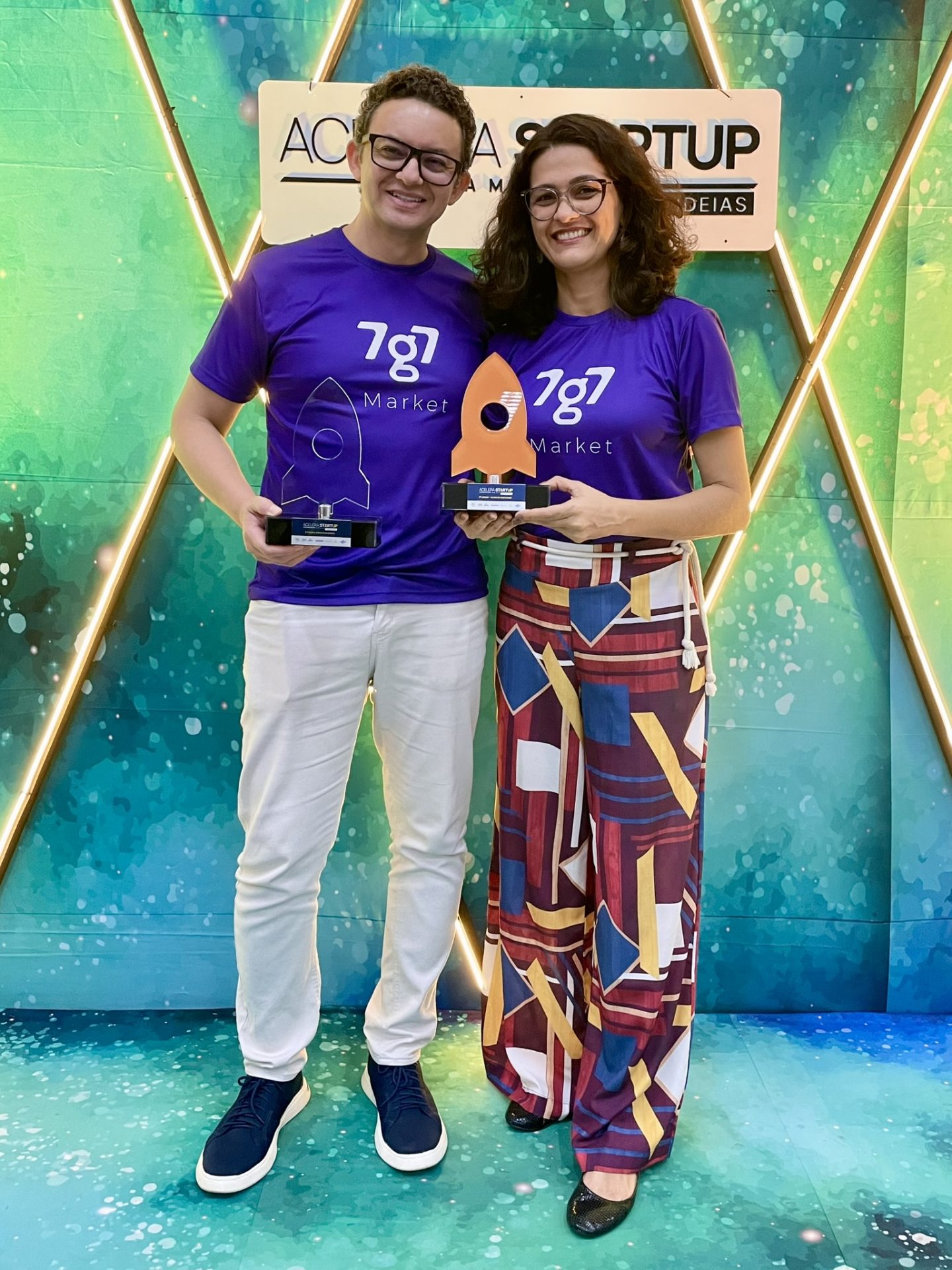 Maikon Richardson e Eryka Tarsylla seguram troféus diante do painel Acelera Startup Amapá, em 2023.
