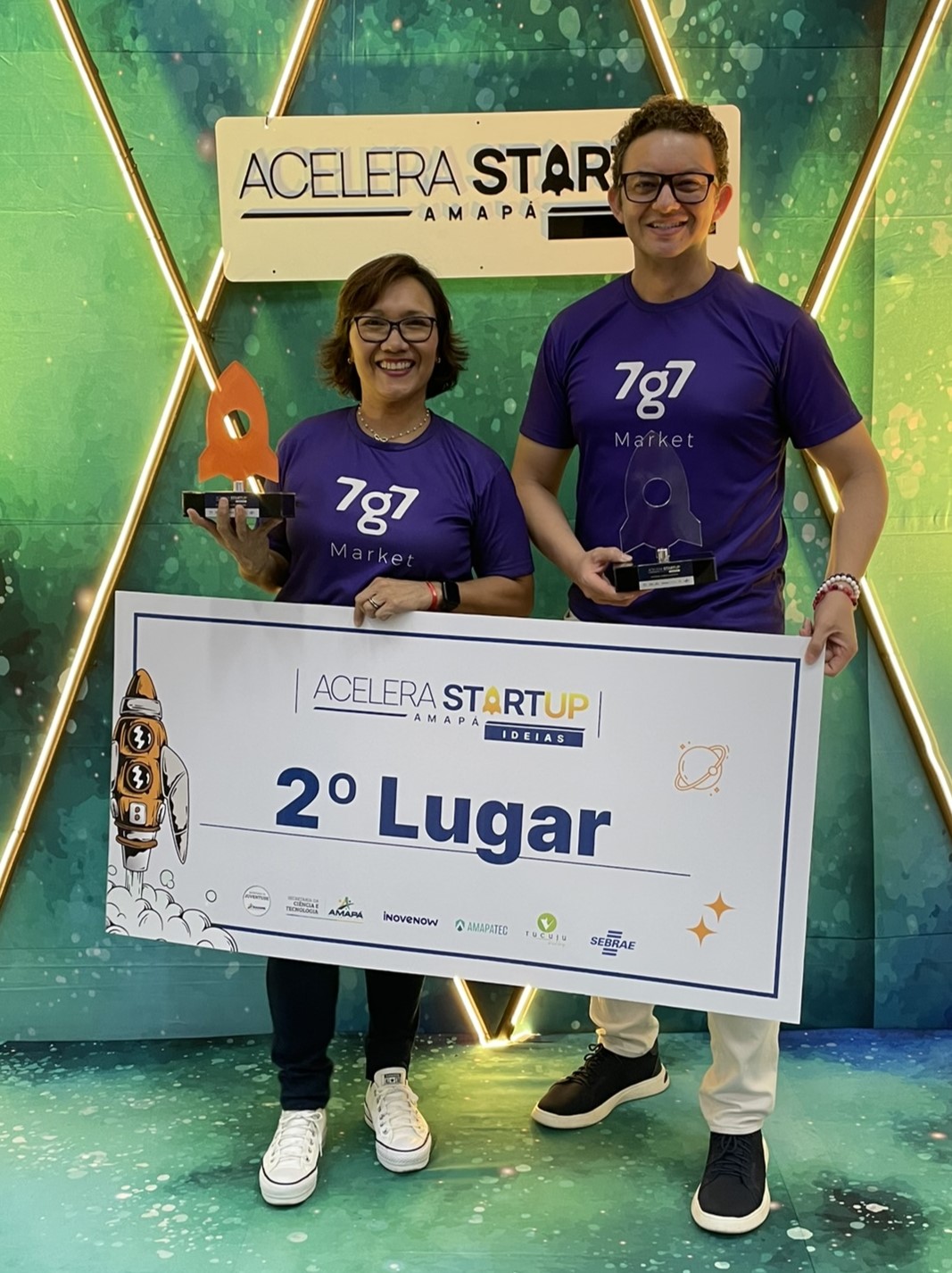 Tania Assunção e Maikon Richardson seguram troféus junto à placa de segundo lugar do Acelera Startup, em 2023.