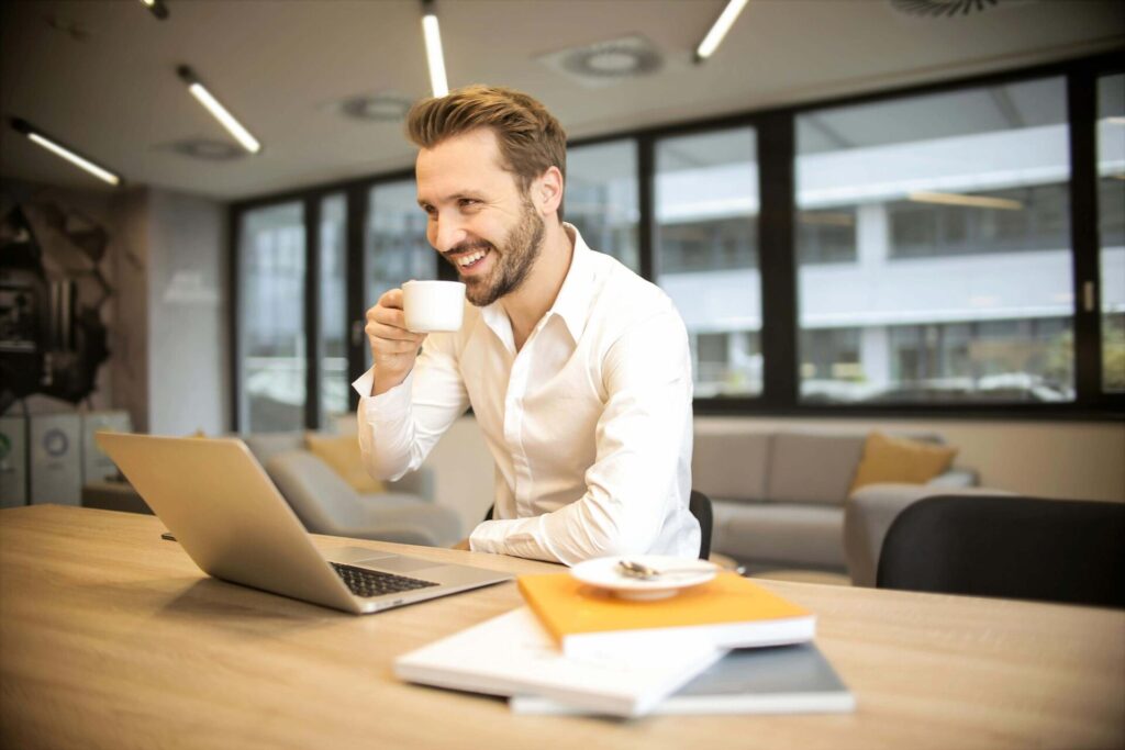 homem feliz tomando café em frente a um notebook enquanto planeja marketing de conteúdo para cafés