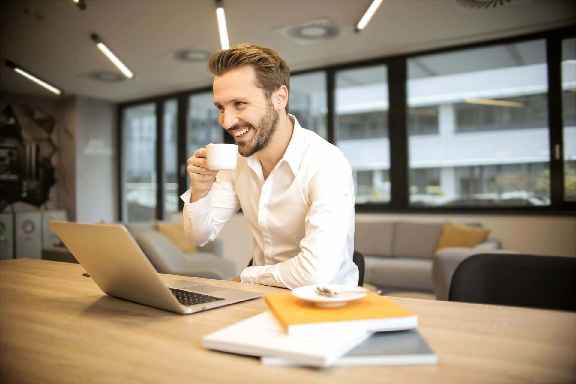 homem feliz tomando café em frente a um notebook enquanto planeja marketing de conteúdo para cafés